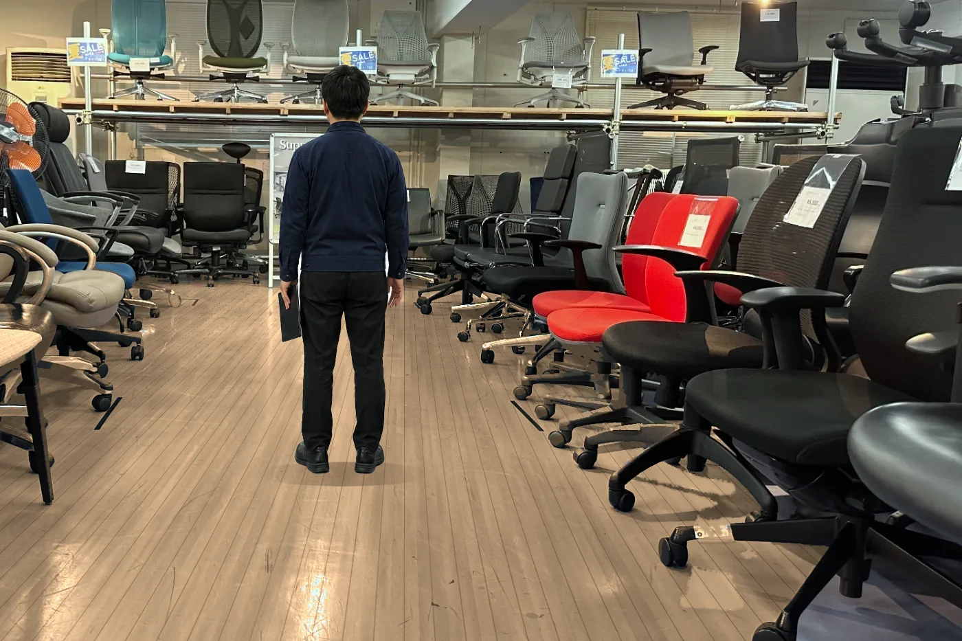 整備済みの中古オフィスチェアが並ぶ通路を確認するスタッフ